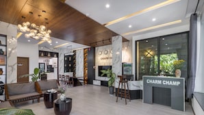 Un hall d’entrée moderne avec un comptoir de réception portant l’inscription « CHARM CHAMP », un espace détente avec des canapés et des tables, et une grande fenêtre donnant sur un paysage verdoyant.
