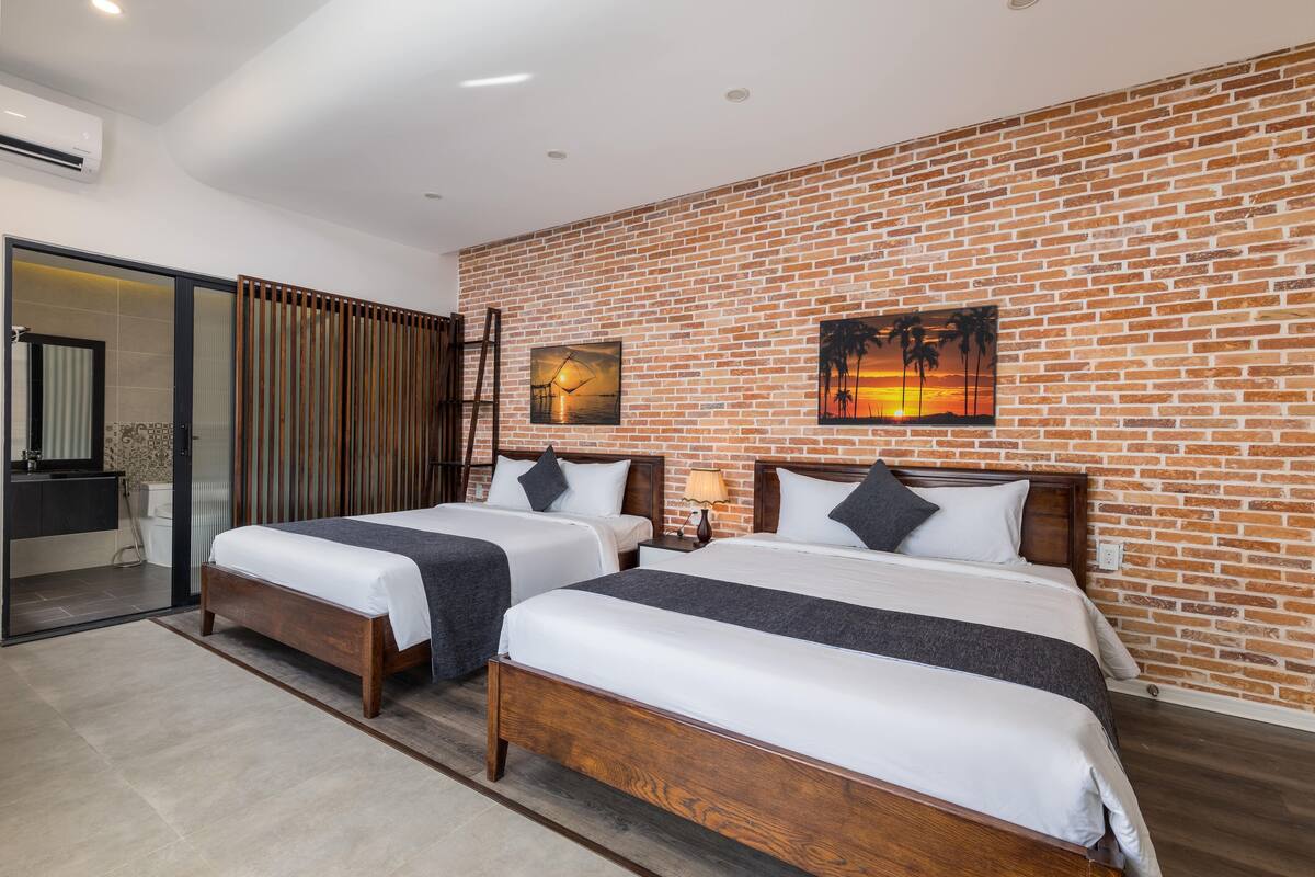 A hotel room with two beds, a brick wall, a painting, and a sliding door to the bathroom.