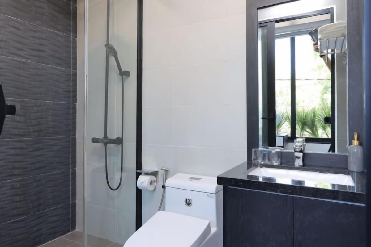 A modern bathroom with a glass-enclosed shower, a white toilet, and a dark-toned vanity with a mirror.