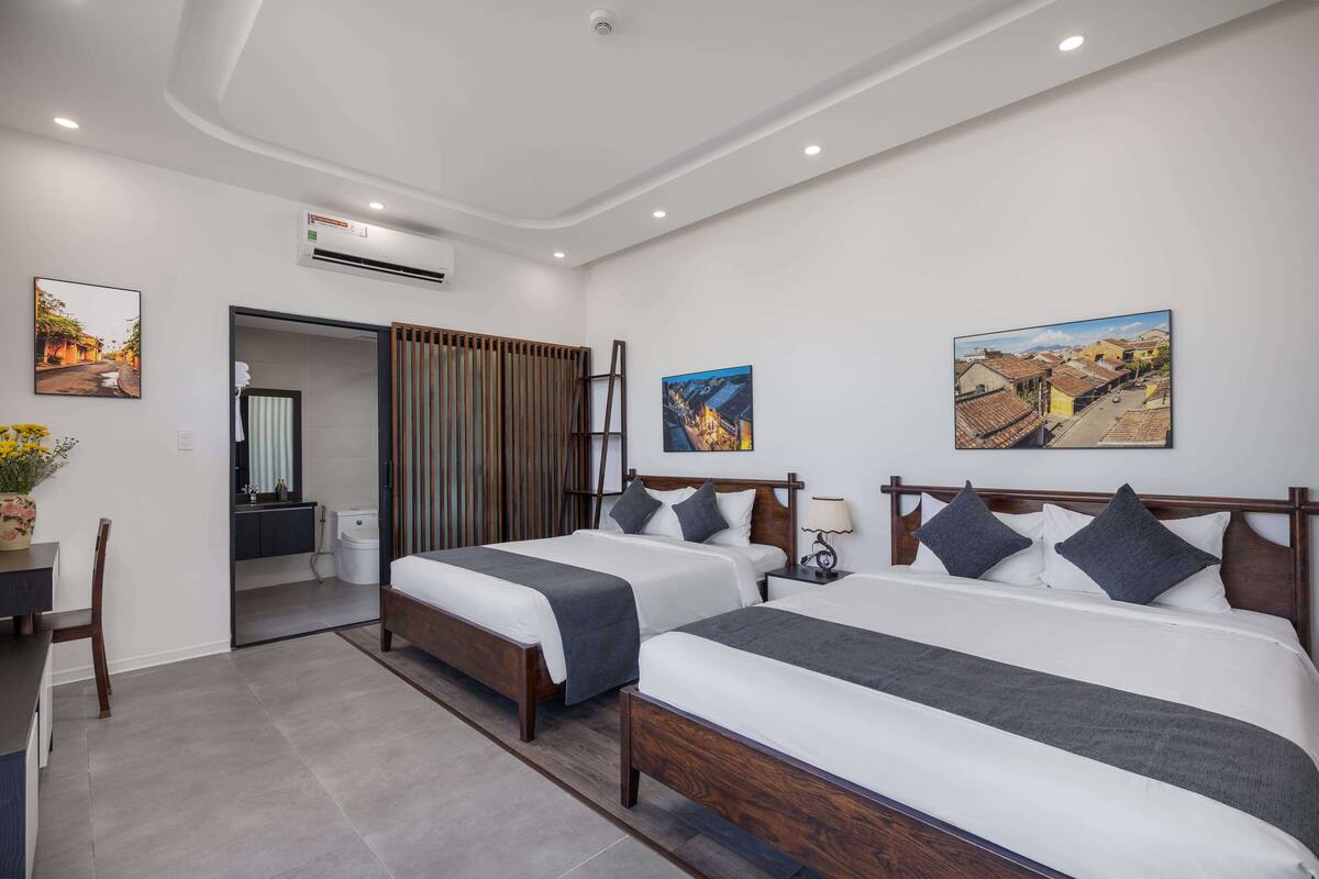A hotel room with two beds, a desk, a chair, and a bathroom.