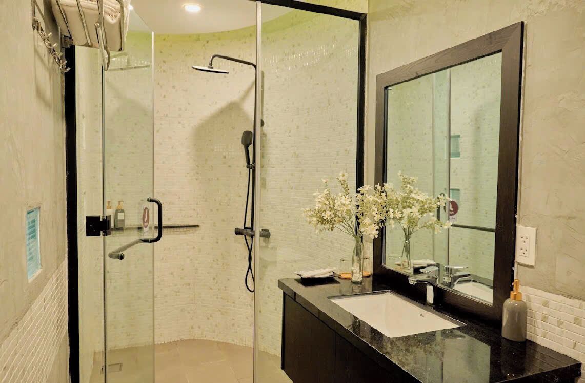 A modern bathroom with a glass-enclosed shower, a black countertop, a large mirror, and a vase with white flowers.