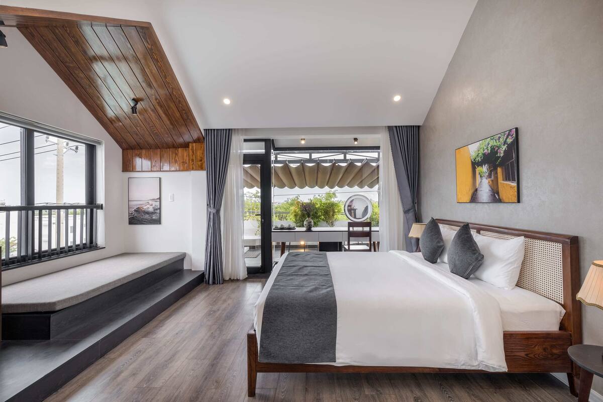 A modern bedroom with a large bed, wooden ceiling, and a view through an open door to an outdoor area.
