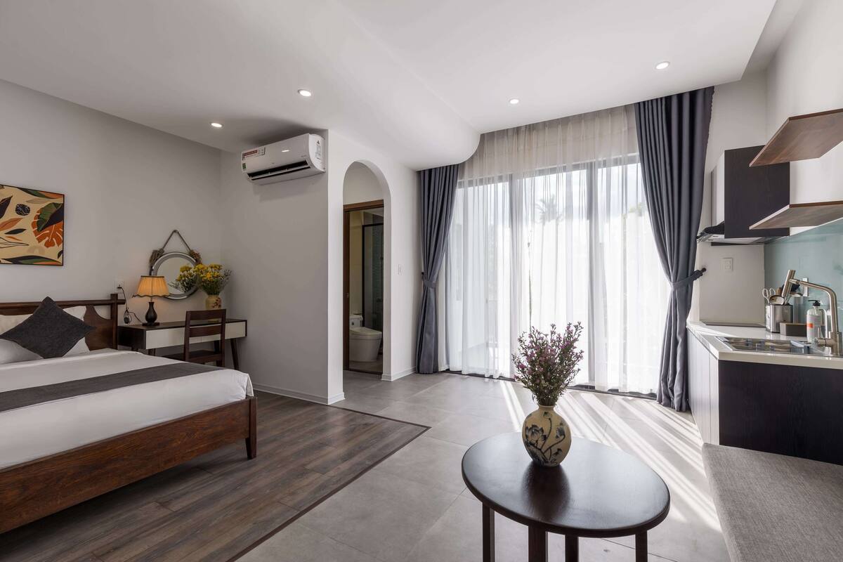 A modern hotel room with a bed, desk, and kitchenette.