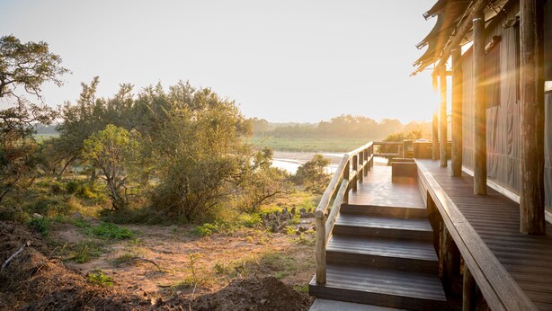 A wooden deck leading to a traditional building with a view of a river and trees.