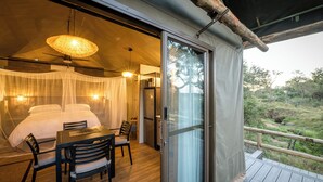 A bedroom with a bed, bedside table, and chairs, a dining area with a table and chairs, and a balcony with a railing.