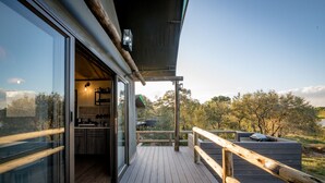 A wooden deck with a glass door leading to a kitchen and a view of trees.