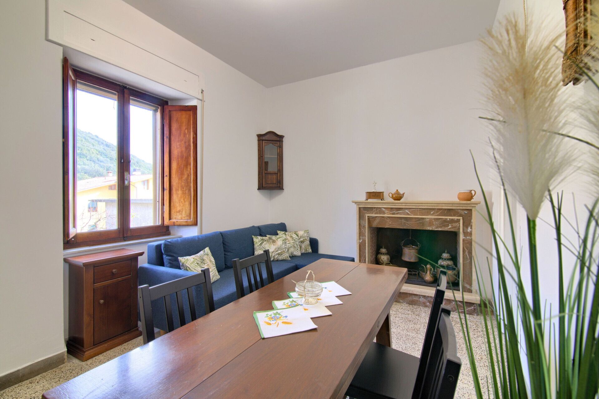 A dining area with a wooden table, blue sofa, and a fireplace with decorative items.