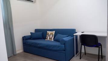 A small, modern room with a blue sofa, a white desk, and a black chair.
