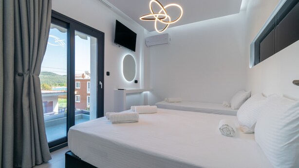 Een moderne hotelkamer met een groot bed, een aan de muur bevestigde televisie en een balkon met uitzicht op gebouwen.