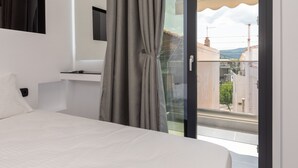Een slaapkamer met een bed, een aan de muur bevestigde televisie en uitzicht buiten via een glazen deur.