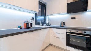 Een moderne keuken met witte kasten, een ingebouwde oven en verlichting onder de kasten.