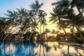 A poolside view with palm trees and a sunset.
