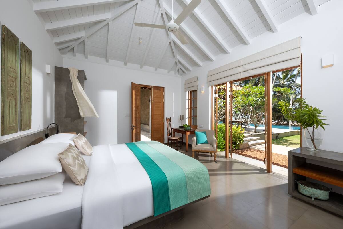 Une chambre à coucher moderne avec un lit, un ventilateur de plafond, un coin repas et une vue sur l’extérieur.