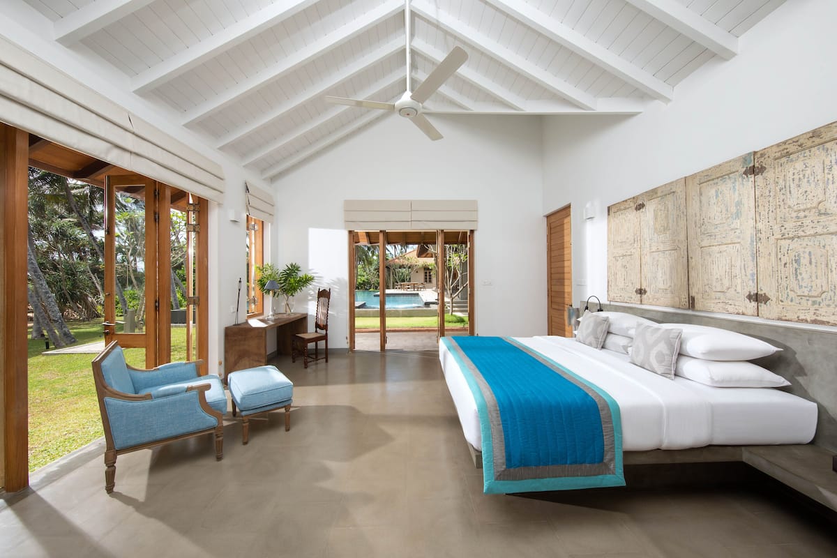 Une chambre spacieuse avec un grand lit, un ventilateur de plafond et une vue sur une piscine.