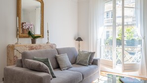 A living room with a grey sofa, a marble console, a large mirror, and a view of a balcony with plants.