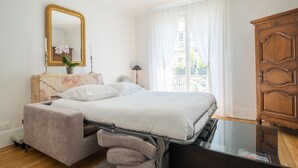 A bedroom with a bed, a vanity with a mirror, a wooden wardrobe, and a window with curtains.