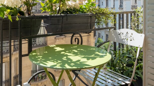 A balcony with a green table, white chairs, and potted plants.