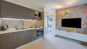 A modern kitchen with grey cabinets, a tiled backsplash, a built-in oven, and a flat-screen TV mounted on the wall. - Casa Gio Near the Waterfall Varone (Riva del Garda)