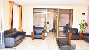 A modern waiting area with leather sofas, a glass coffee table, and a sliding glass door leading to another room. - DIVINE HOMES RESORT KISUMU (Kisumu)