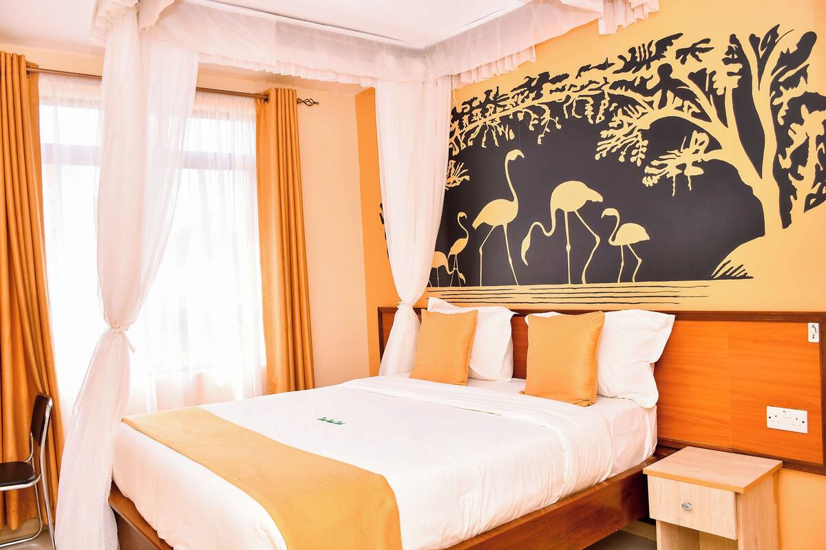A hotel room with a large bed, a nightstand, and a wall mural.