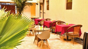 A dining area with tables and chairs, a palm plant, and patterned flooring. - DIVINE HOMES RESORT KISUMU (Kisumu)