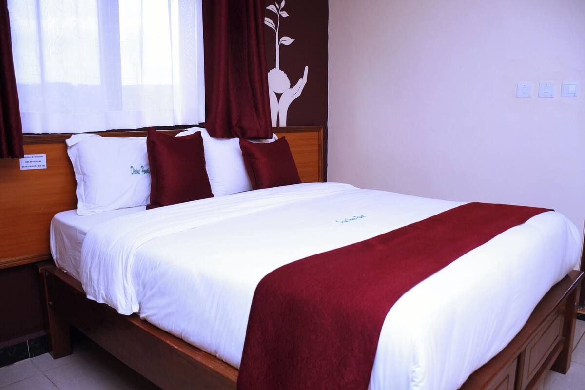 A neatly made bed with white and red bedding, a wooden headboard, and a wall with a white silhouette decoration.