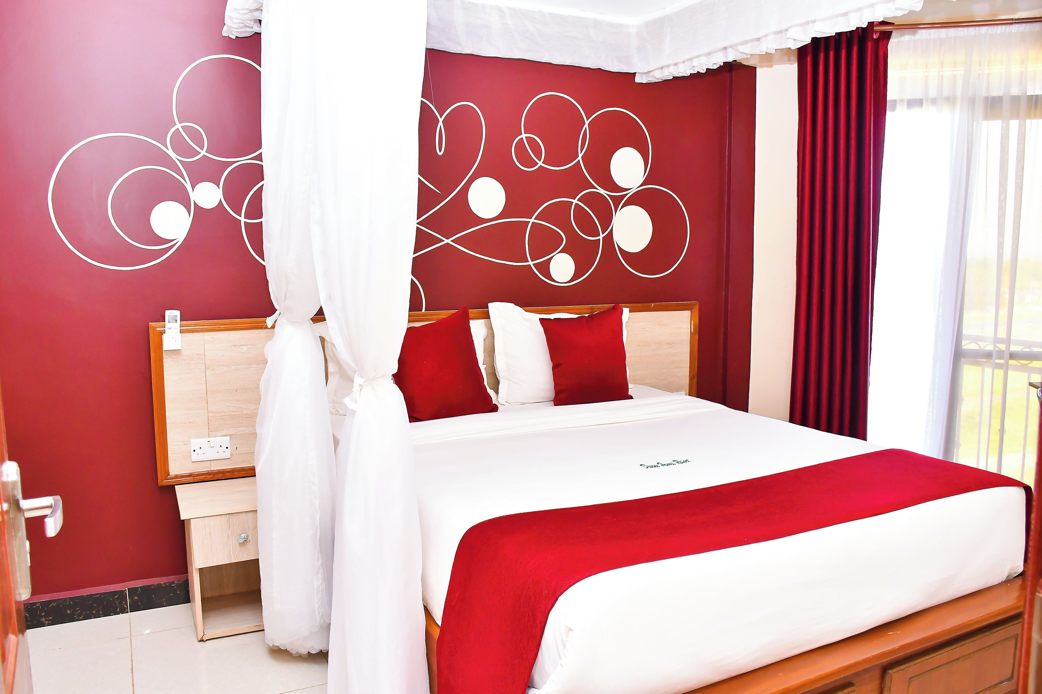 A bedroom with a bed, a nightstand, a mirror, and a red wall with white abstract designs.