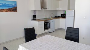 A compact kitchen with white cabinets, a microwave, a coffee maker, and a dishwasher. There is a dining table with a white tablecloth and two chairs. - Immaculate 2-bed Apartment in Okrug Gornji (Okrug)