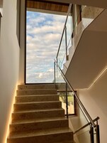 Una escalera moderna con barandillas de cristal y vista al cielo a través de un ventanal grande.