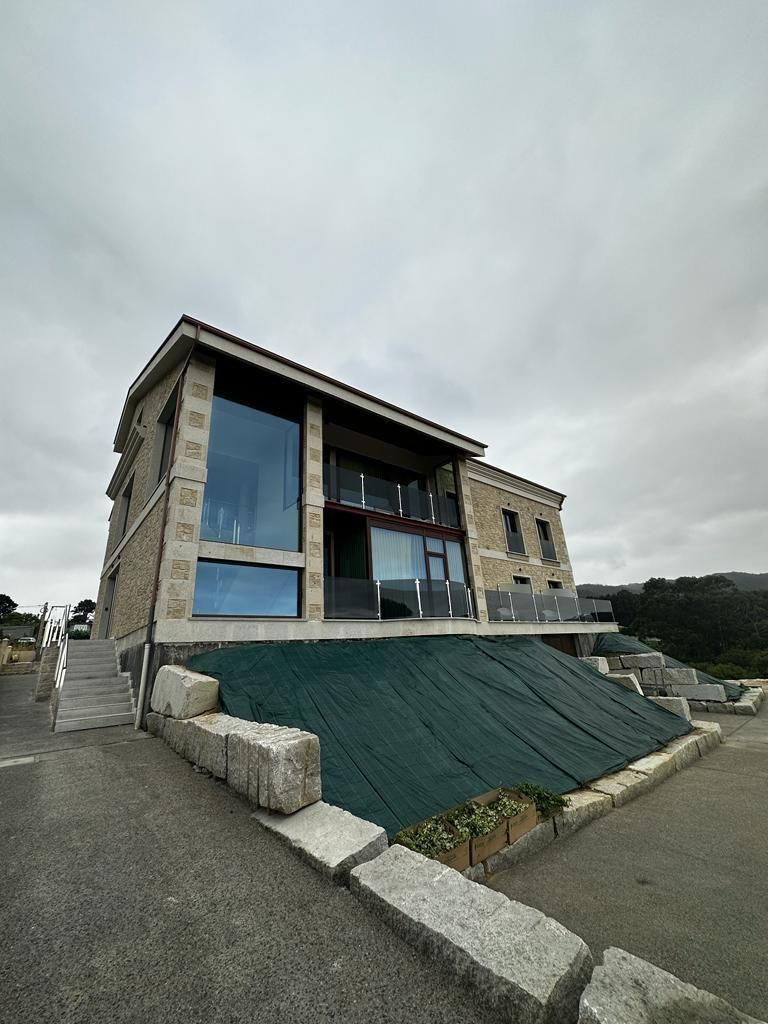 A two-story building with a flat roof, large windows, and a green tarp covering the ground.
