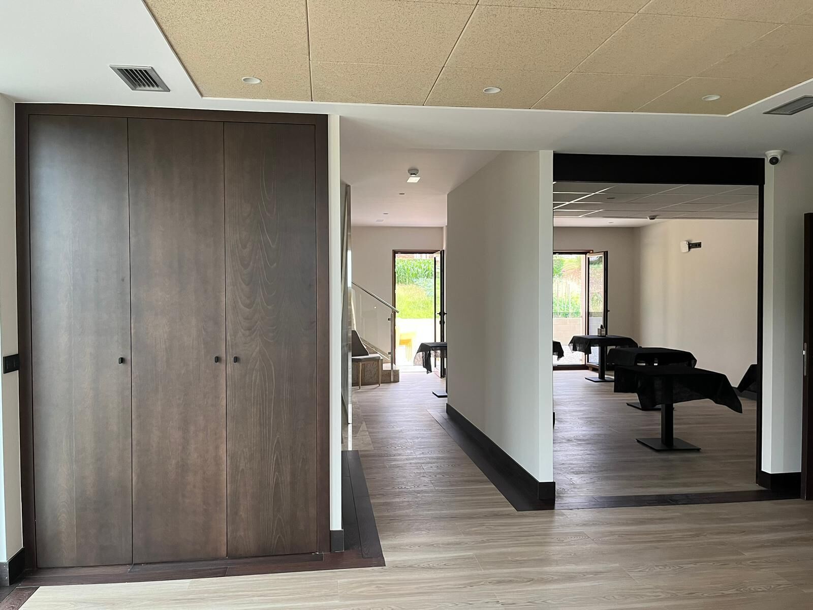 A modern hotel corridor with a wooden door, a staircase, and a seating area with tables and chairs.