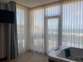 Una habitación de hotel con un ventanal grande, un jacuzzi y un televisor de pantalla plana.