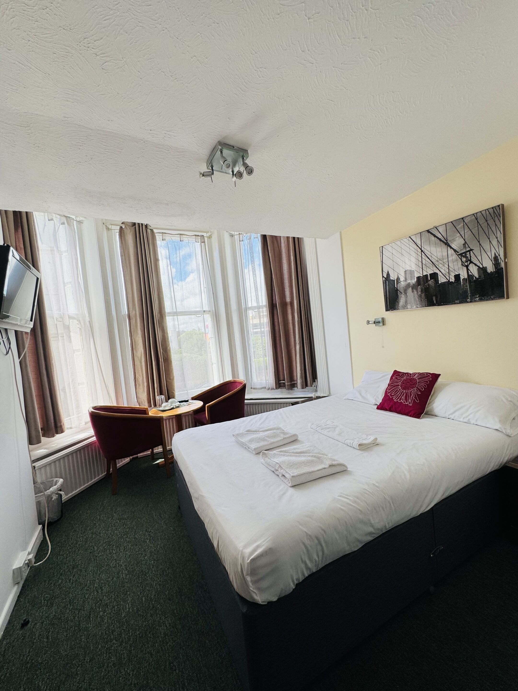 Habitación de hotel con cama, escritorio, silla, televisor y ventana con cortinas.