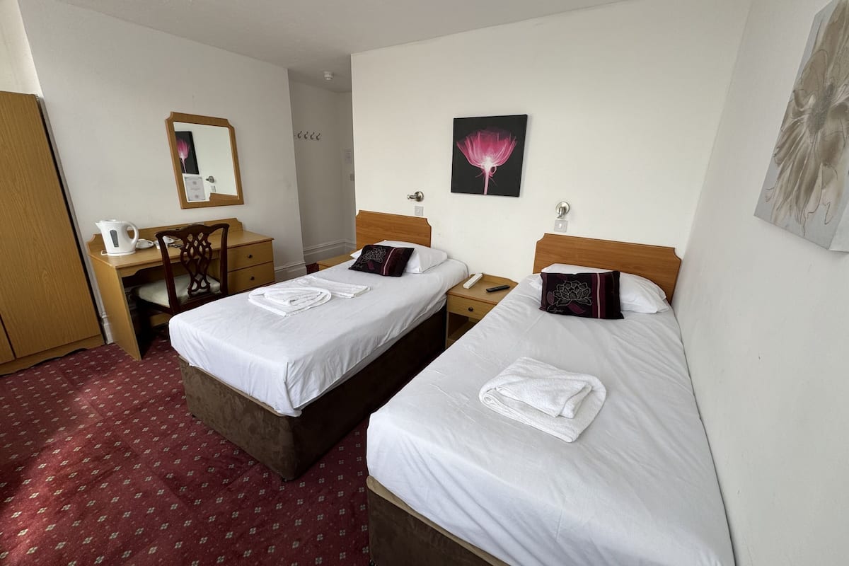 Een hotelkamer met twee bedden, een bureau, een stoel, een spiegel en een schilderij aan de muur.