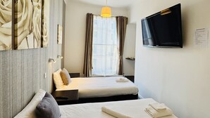 A hotel room with two beds, a TV mounted on the wall, a window with curtains, and a painting on the wall.