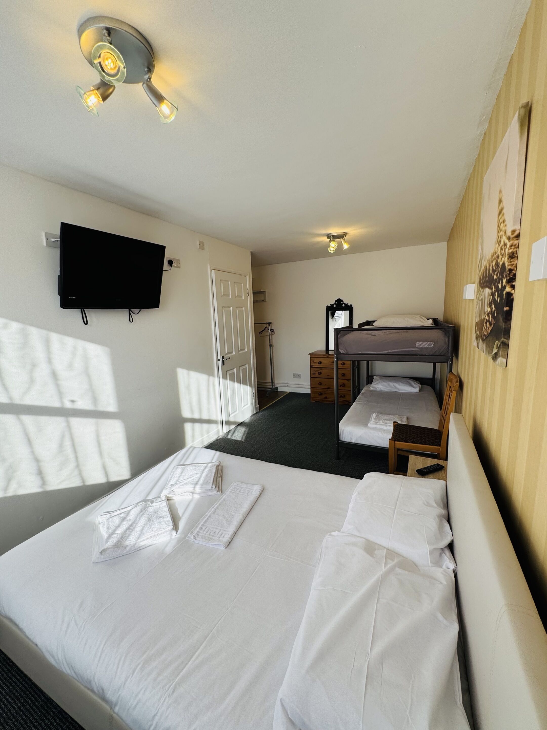Une chambre d’hôtel équipée d’un lit, d’un bureau, d’une chaise, d’un téléviseur fixé au mur et d’un luminaire au plafond.