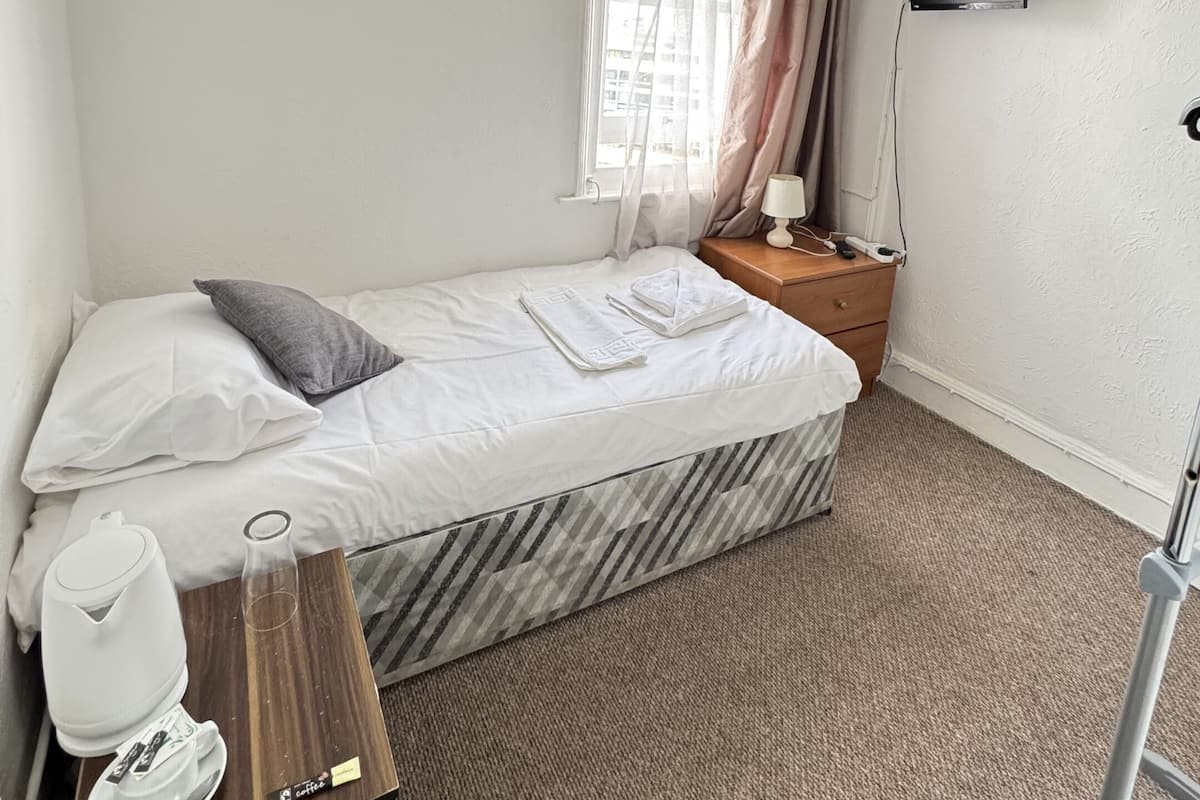 Een compact, netjes ingerichte slaapkamer met een bed, nachtkastje met lamp, televisie aan de muur en een raam met gordijnen.