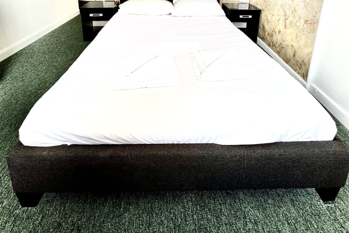 Een netjes opgemaakt bed in een hotelkamer met een wand in marmerlook, een klein nachtkastje en een nachtlampje.
