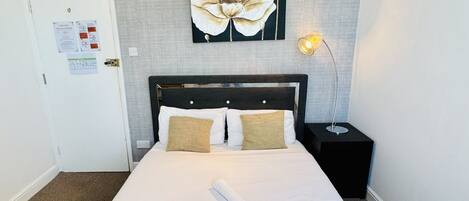 A neatly made bed with white linens, two pillows, and two folded towels.