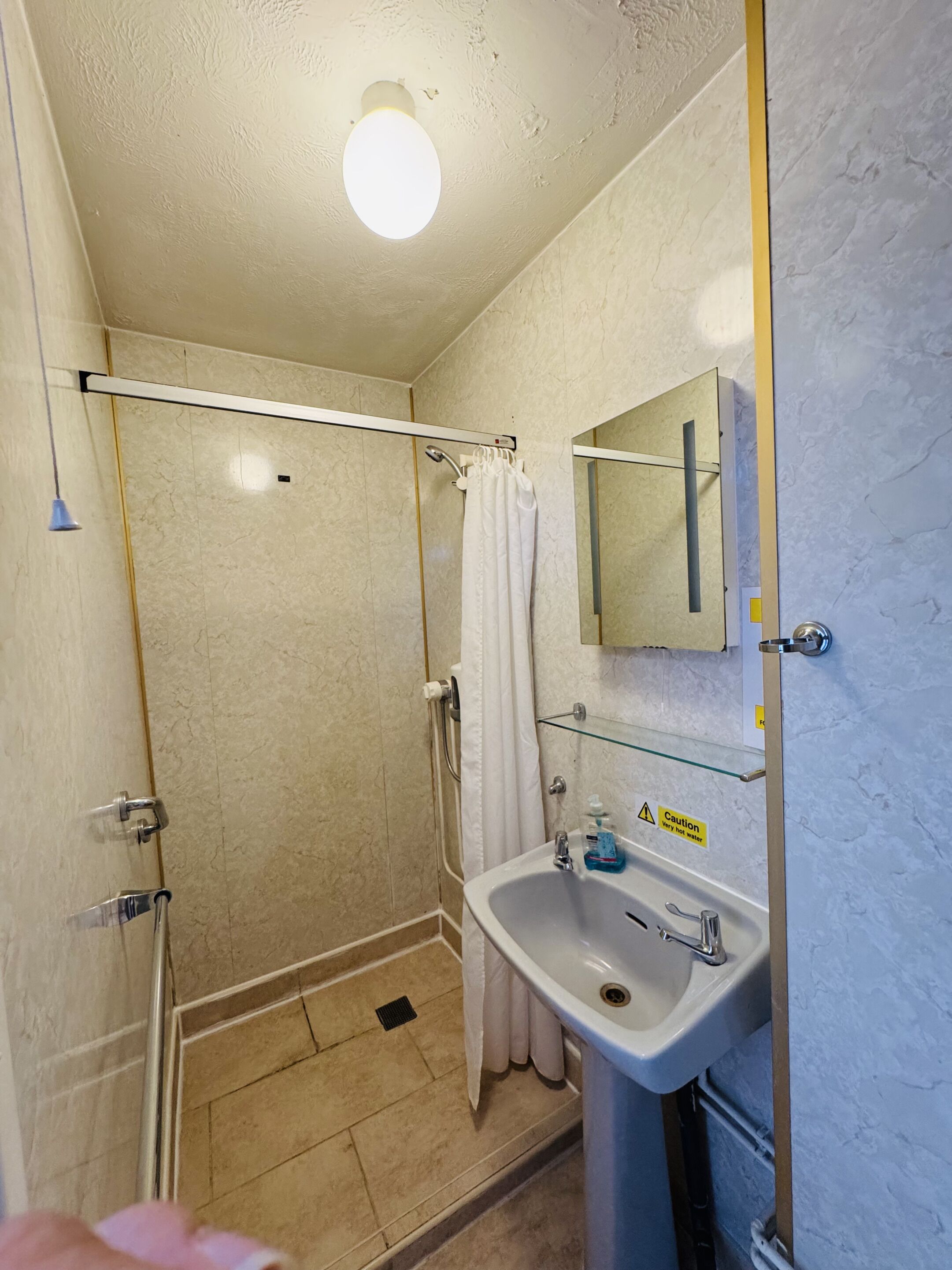 A bathroom with a glass shower enclosure, a white sink, and a mirror above it.