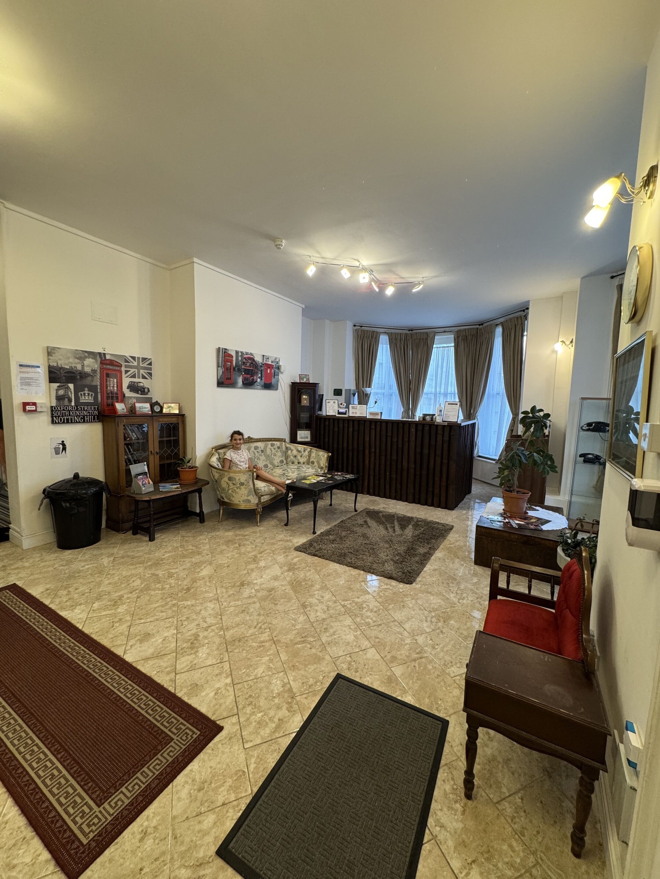 Amplia sala de estar con sofá, una mesa de centro y una alfombra. Se observa un mueble con adornos y un cesto de basura.