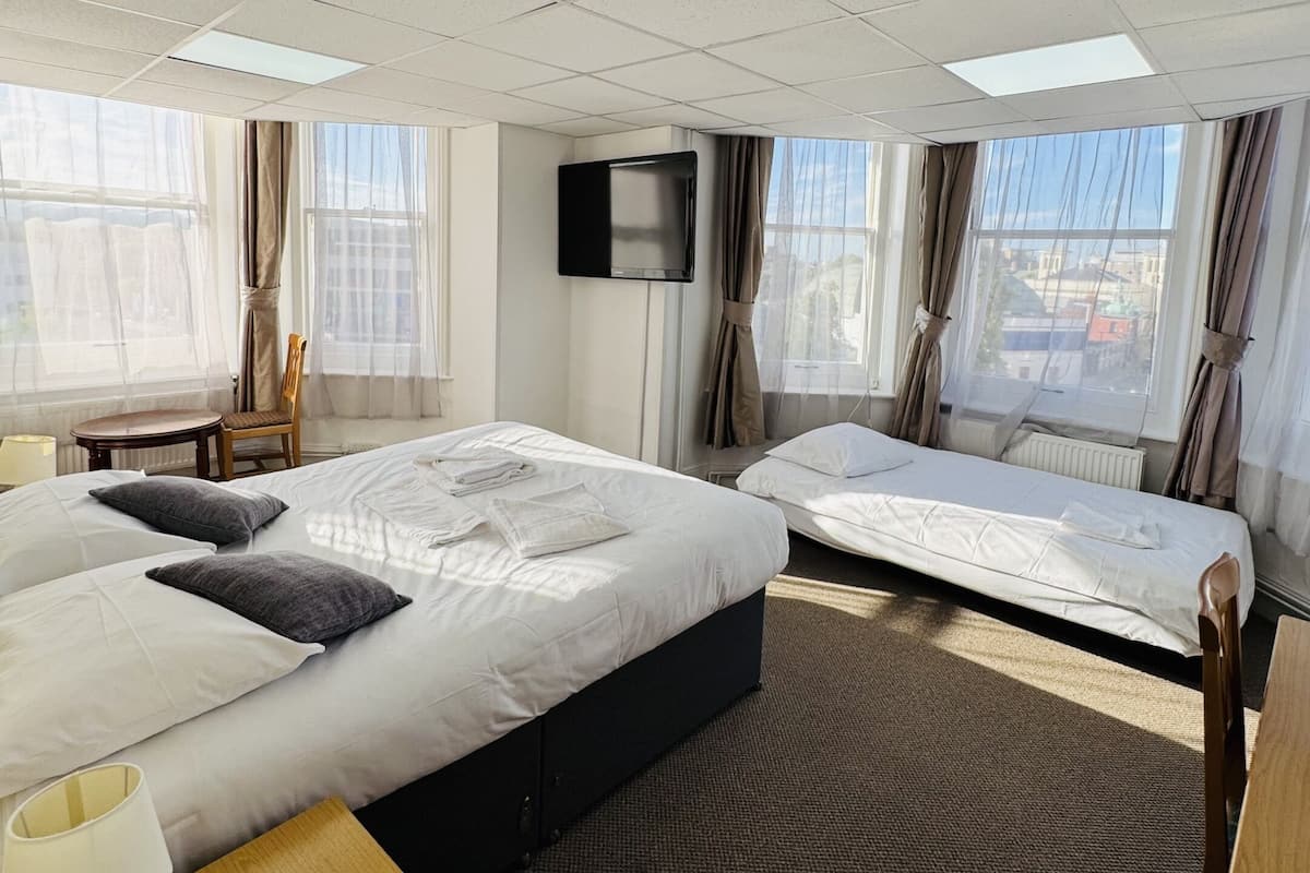 Een hotelkamer met een groot bed, een kleiner bed, een televisie en een raam met gordijnen.