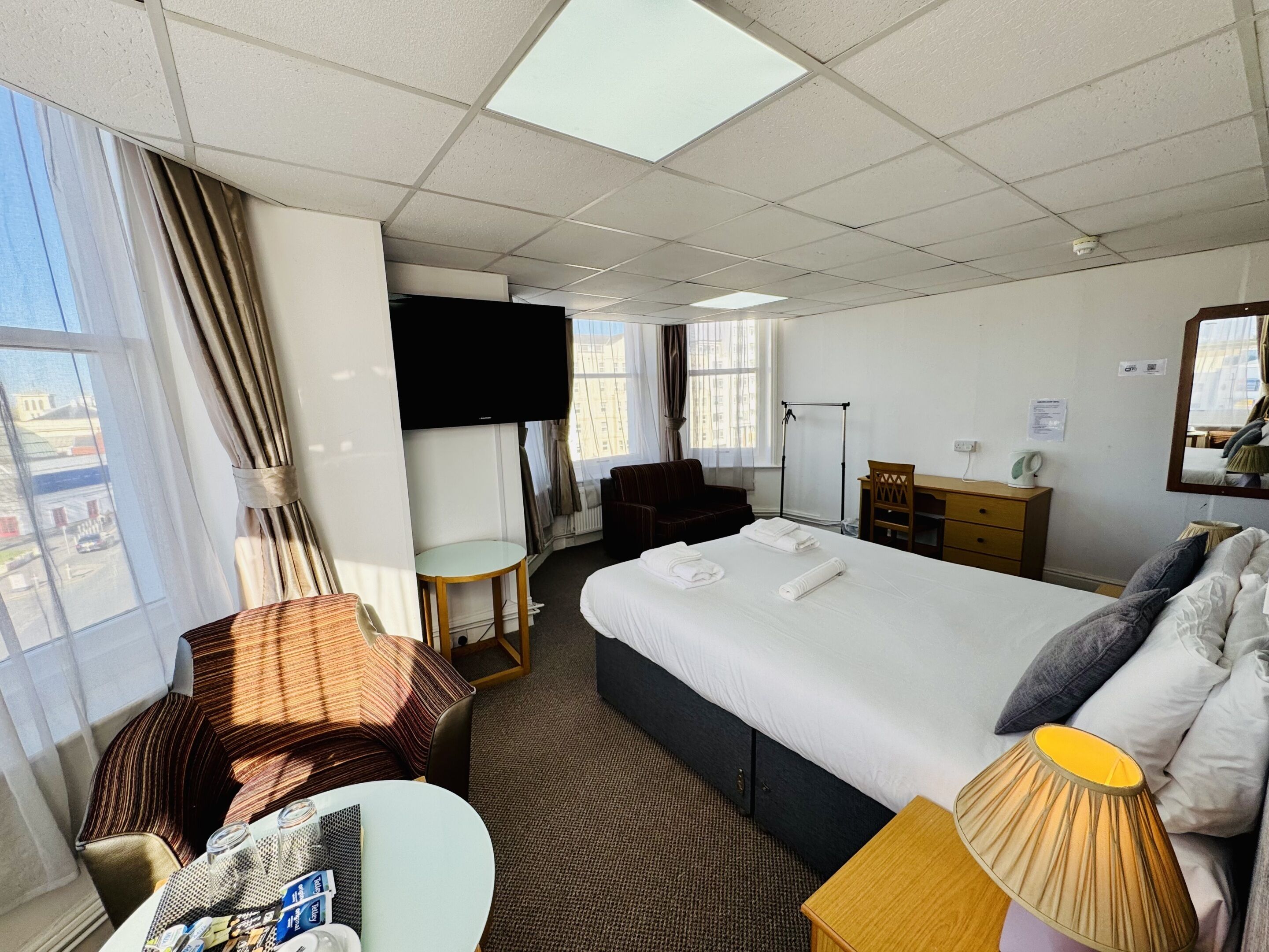 A hotel room with a bed, a desk, a chair, a TV, and a window with curtains.