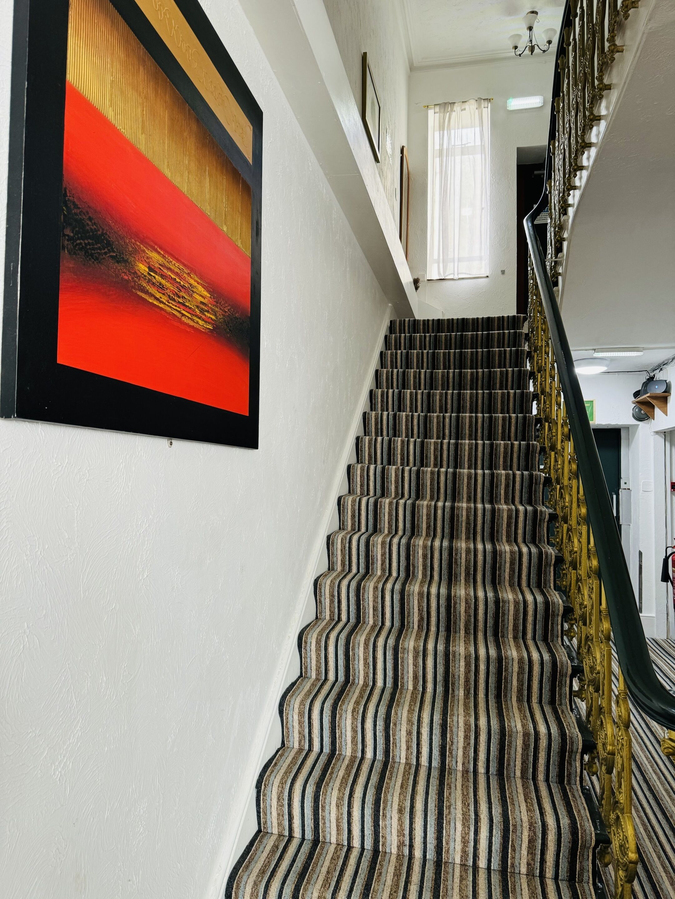 A staircase with a patterned carpet, a framed artwork on the wall, and a chandelier.