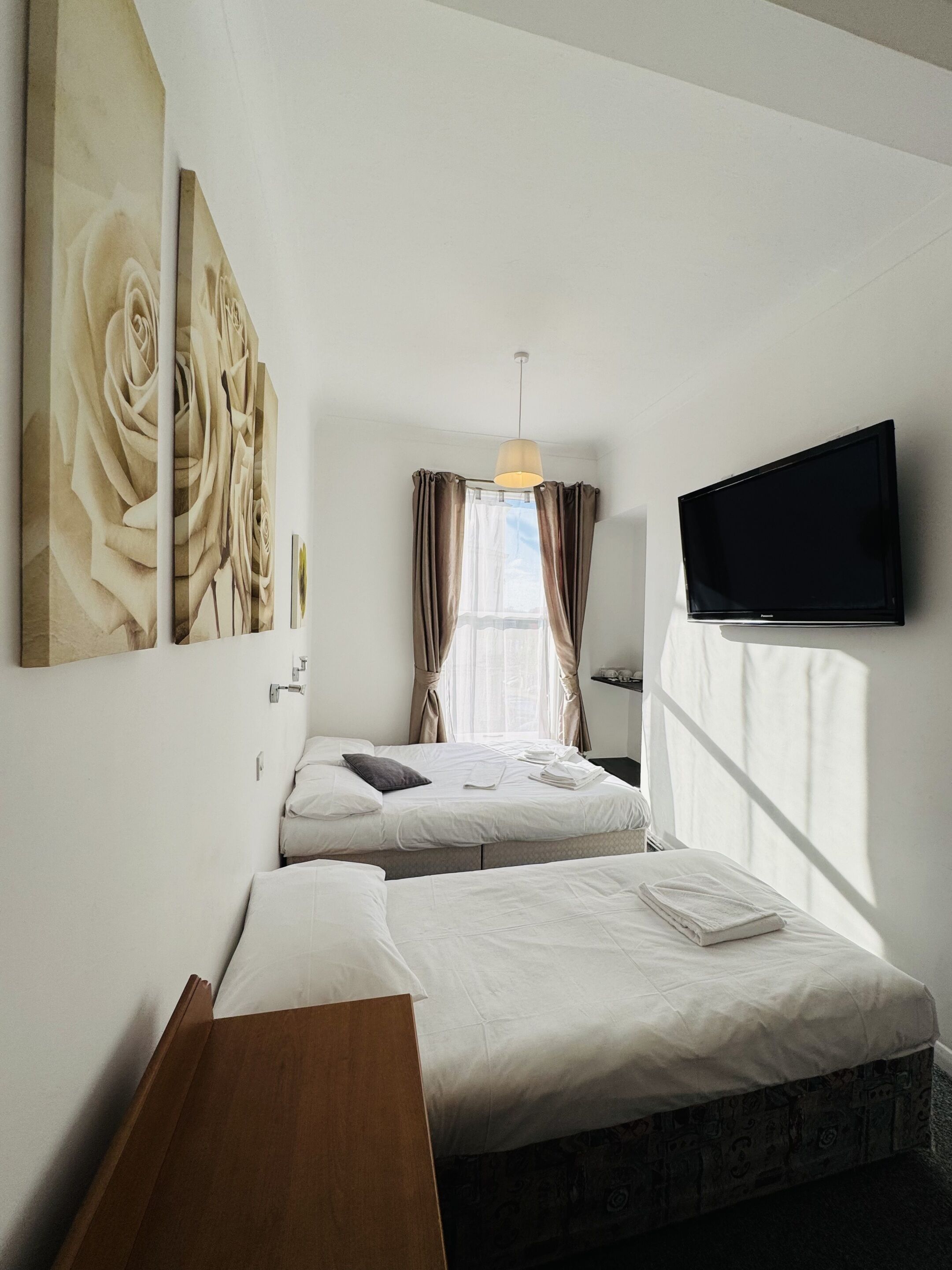 Quarto de hotel com duas camas, televisão de tela plana na parede e uma janela grande com cortinas.