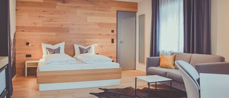 A modern bedroom with a wooden headboard, a bed with white bedding, a grey sofa, a small table, and a leather rug.