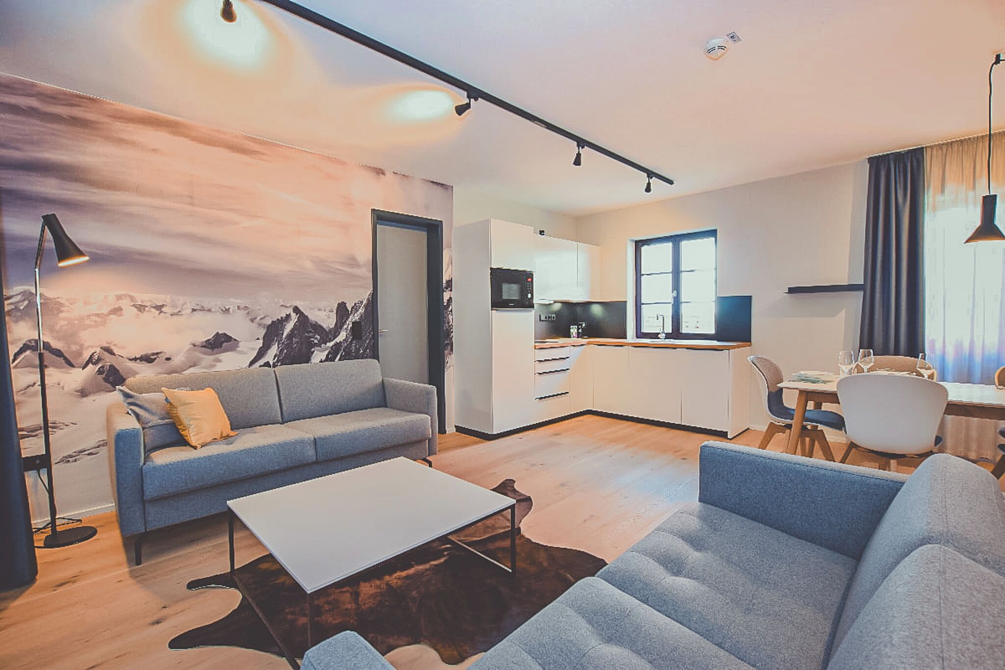 A modern living room with a sofa, coffee table, and a large painting of mountains.