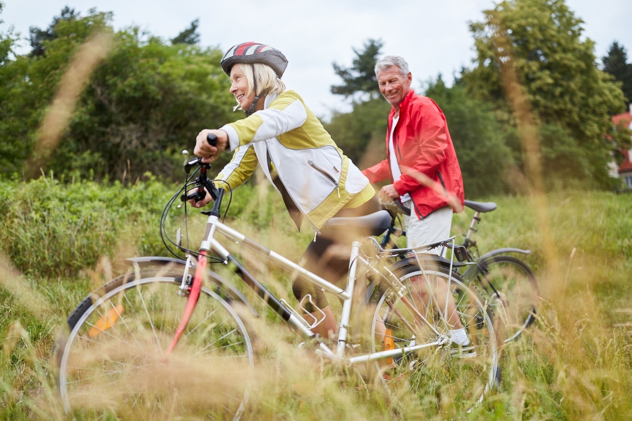 Dos personas paseando en bicicleta por un campo con árboles al fondo.