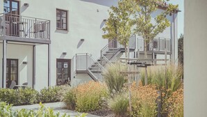 Ein modernes Gebäude mit Balkon, Sitzgelegenheiten im Freien und einem Gartenbereich mit Blumen und Pflanzen.