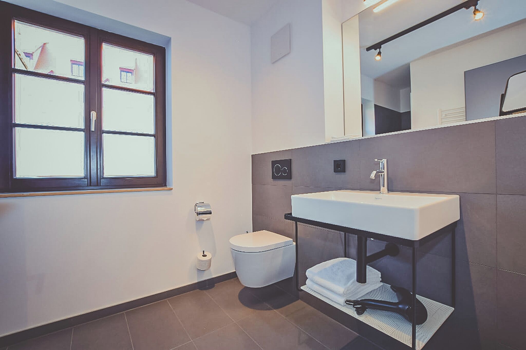 A modern bathroom with a toilet, sink, and window.